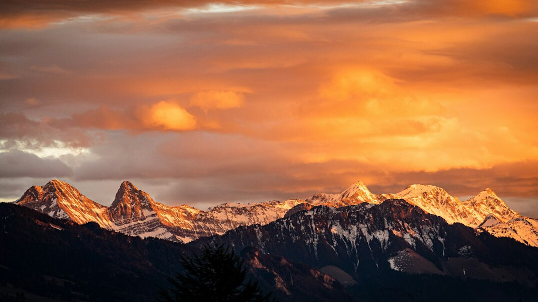 Dramatic Swiss mountain range glowing orange at sunset with low clouds