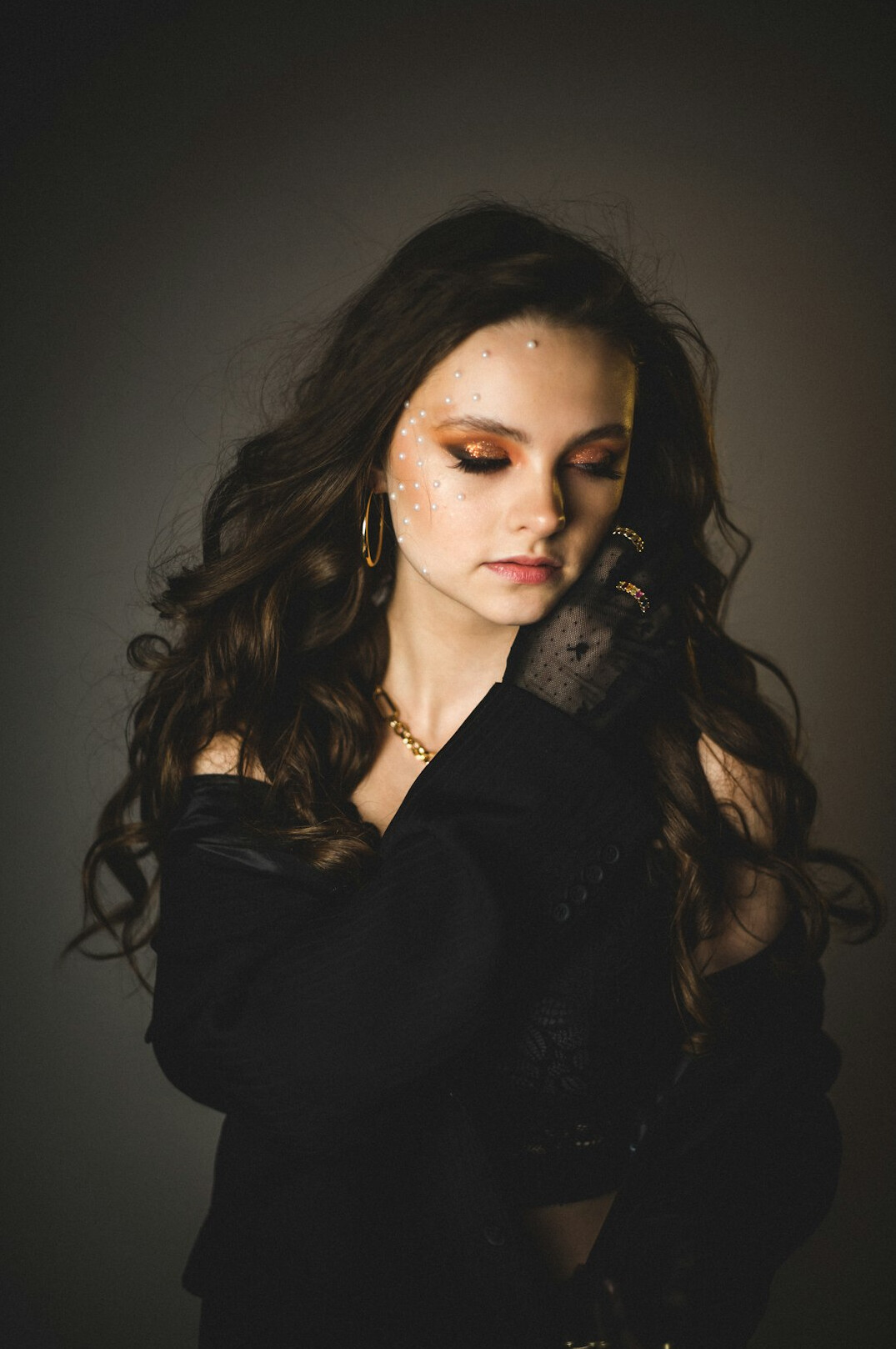 Studio portrait of a 32 year old white female pop singer with wavy hair and gold jewelry